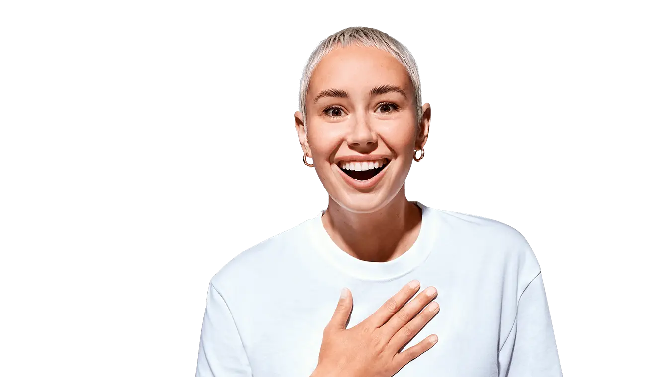 Eine lächelnde Person mit kurzem blondem Haar und hellem Hemd, die eine Hand vor die Brust legt und überrascht, begeistert blickt.